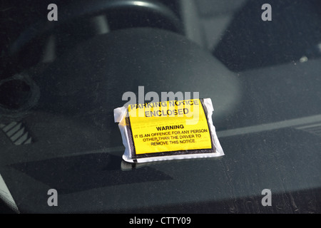 A parking violation notice has been placed onto a cars dirty windscreen. Stock Photo