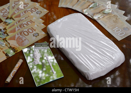 Large bag of cocaine and coke line with razor blade on mirror on table with Canadian 100 dollar bills cash money Stock Photo