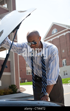 A business man having a bad day checks under the hood of his car to figure out what the problem is. Stock Photo