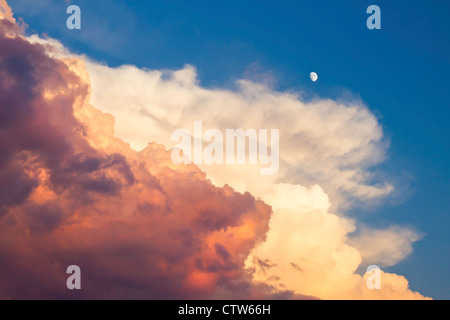 Colorful puffy storm clouds and moon at sunset. Stock Photo