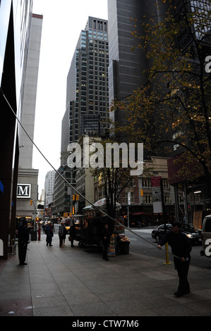 Autumn sidewalk portrait, to 7th Avenue, man bending telescopic squeegee cleaning facade Chase Bank. West 52nd Street, New York Stock Photo