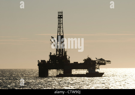 silhouette of an offshore oil drilling rig. Helicopter landed and supply vessel alongside. Stock Photo
