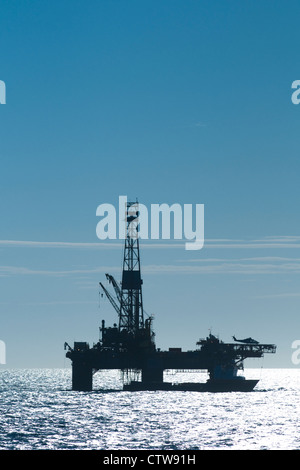 silhouette of an offshore oil drilling rig. Helicopter landed and supply vessel alongside. Stock Photo
