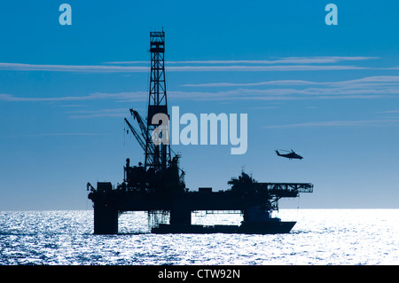 Silhouette of an oil drilling rig in offshore area.  Helicopter departing from it. Stock Photo