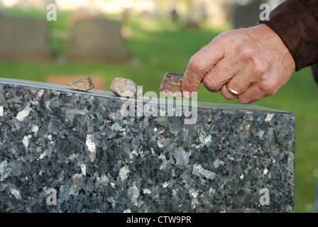 Man's hand placing a stone on top of a headstone in a cemetery. Stock Photo