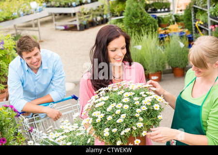 Florist assisting young woman choose flowers at garden shopping center Stock Photo