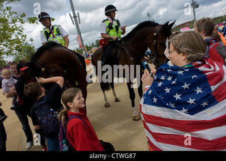 American spectators admire mounted police officers on horseback help control crowds and provide security in the Olympic Park during the London 2012 Olympics. This land was transformed to become a 2.5 Sq Km sporting complex, once industrial businesses and now the venue of eight venues including the main arena, Aquatics Centre and Velodrome plus the athletes' Olympic Village. After the Olympics, the park is to be known as Queen Elizabeth Olympic Park. Stock Photo