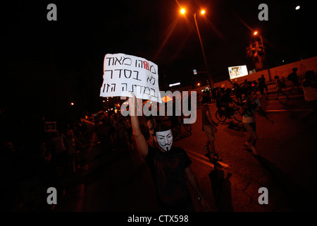 An Israeli protester wearing a Guy Fawkes mask used by the anonymous movement holds a paperboard sign reading 'Something is totally wrong in this country' during Cost of Living protest in Tel Aviv Israel. The social justice protest also named the Tents protest protest  were a series of demonstrations in Israel beginning in July 2011 involving hundreds of thousands of protesters from a variety of socio-economic opposing the continuing rise in the cost of living particularly housing. Stock Photo