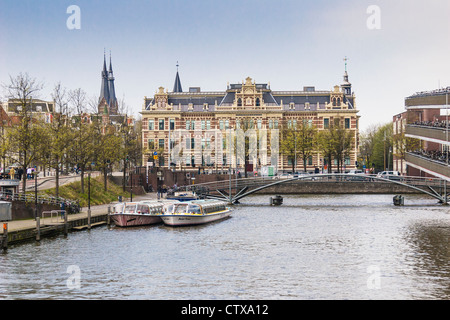 City of Amsterdam harbor canals with Central train station bicycle parking garage and tourist canal tours boats, in South Holland, The Netherlands. Stock Photo