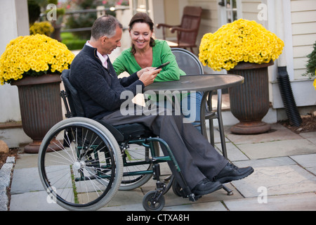 Woman and her husband in a wheelchair sitting at a cafe and using a digital tablet Stock Photo