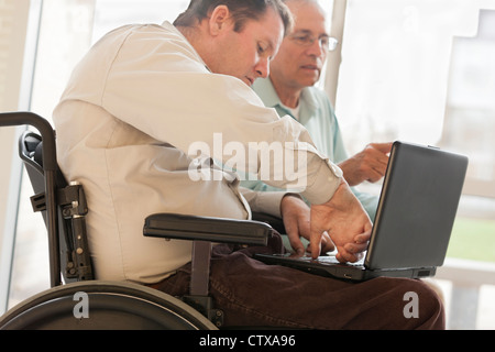Quadriplegic man with spinal cord injury in wheelchair using his thumb to type on computer Stock Photo