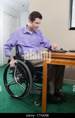 Man in wheelchair with spinal cord injury using his electronic tablet for e-mail; quadriplegic issue with hand dexterity Stock Photo