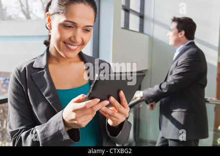 Businesswoman looking at tablet with businessman behind her Stock Photo