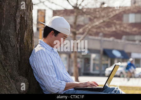 Chinese student sitting under a tree using laptop Stock Photo