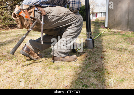 Hispanic carpenter measuring from corner of house to use post hole digger Stock Photo
