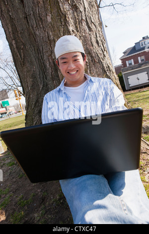 Chinese student sitting under a tree using laptop Stock Photo