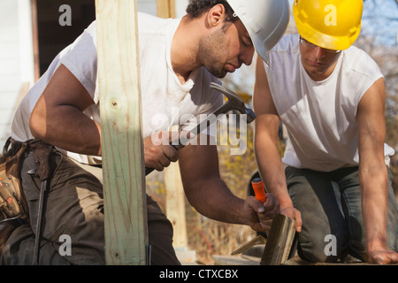 Hispanic carpenters using hammer and chisel on deck support Stock Photo