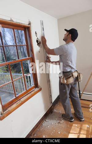 Hispanic carpenter using level to mark cut for new deck doorway in house Stock Photo