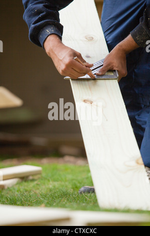 Hispanic carpenter using square to mark cut on board for construction Stock Photo