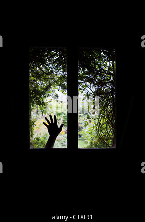 Silhouette hand against Glass windows in a front door in front of a Overgrown garden view. UK Stock Photo