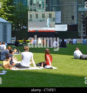 Office workers taking lunch time break watching large screen outdoor BBC news broadcast Stock Photo