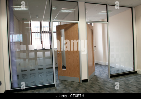 Open doors leading to two empty offices behind frosted glass panels in a modern open-plan office and call centre Stock Photo