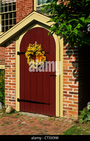 Spring Forsythia wreath on a colonial brick house vintage red door PT image near Rochester, New York, USA, US upstate Stock Photo