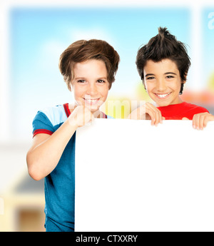 Happy schoolboys in the classroom, cheerful preteen boys students holding white blank board with copy space for ad text Stock Photo
