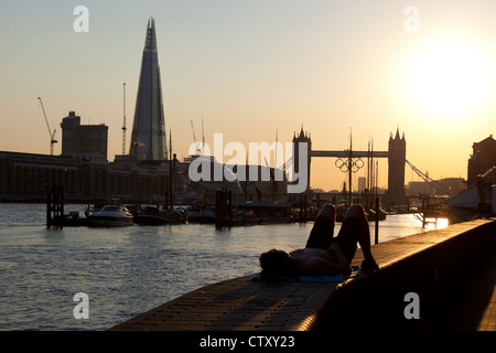 A man relaxing on the Thames path with The Shard & Tower Bridge decorated with the Olympic Rings in the background, London, UK. Stock Photo