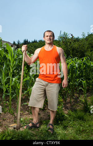 Sweating working young farmer with a hoe near a corn field Stock Photo