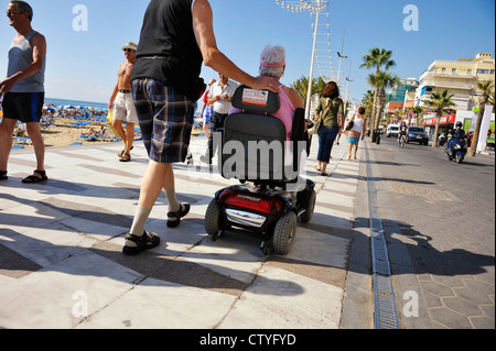 man accompanies woman on electric scooter on Levante beach promenade in Benidorm, Spain Stock Photo