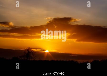 Sun breaks through the clouds showing its rays of light at sunset Stock Photo