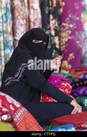 Muslim woman, with hidden face behind veil, selling clothes in her own business shop Stock Photo