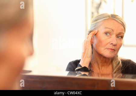 Older woman applying makeup in mirror Stock Photo