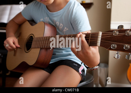 Japanese-American 10 year old girl practices playing guitar, uses sheet music while at home. Stock Photo