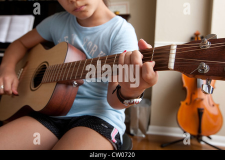 Japanese-American 10 year old girl practices playing guitar, uses sheet music while at home. Stock Photo