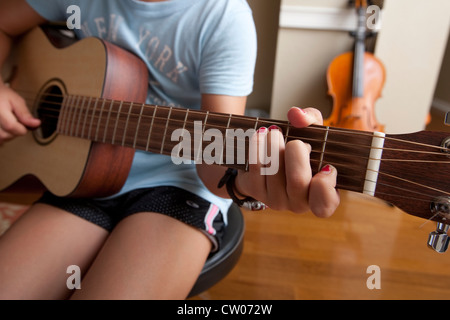 Japanese-American 10 year old girl practices playing guitar, uses sheet music while at home. Stock Photo