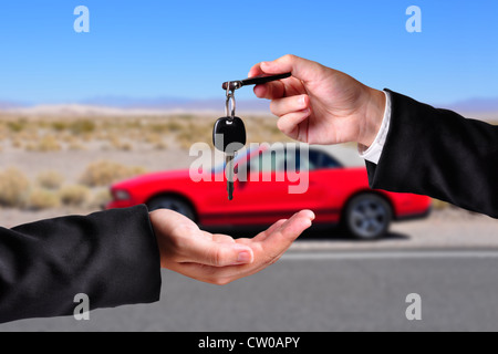 A hand giving a key to another hand. Both persons in suits. Car in the background. Stock Photo