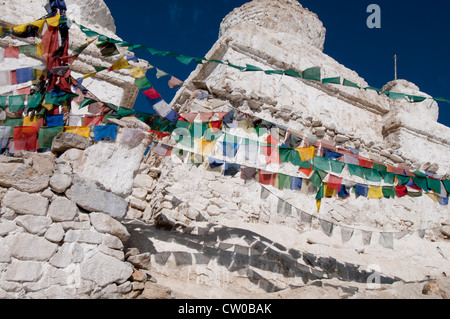 Portion of a white-washed stone wall at Shey Monastery with stings of brightly colored prayer flags hanging against it. Stock Photo