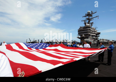 Sailors hold up the national ensign on the flight deck of the Nimitz-class aircraft carrier USS Abraham Lincoln (CVN 72) during an air power demonstration. Lincoln is en route to the United States to complete an eight-month change-of-homeport deployment during which it operated in the U.S. 5th, 6th and 7th Fleet areas of responsibility. Stock Photo