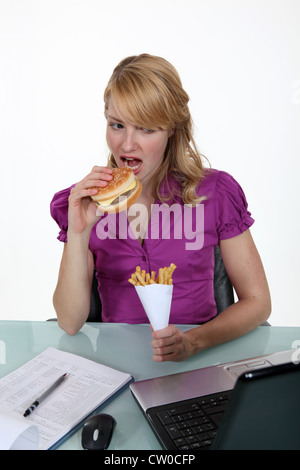 Woman eating junk food at her desk Stock Photo