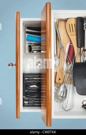 Open Kitchen Drawer with utensils on display with light blue background Stock Photo