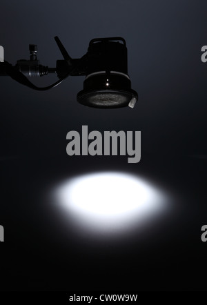 A photographic light from above creating a white spotlight on an empty dark background.
