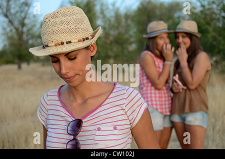 Two friends gossiping at the back of another sad friend Stock Photo