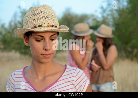 Two friends gossiping at the back of another sad friend Stock Photo