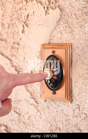 A visitor pushing a brass, antique doorbell that's mounted to a stucco wall. Stock Photo