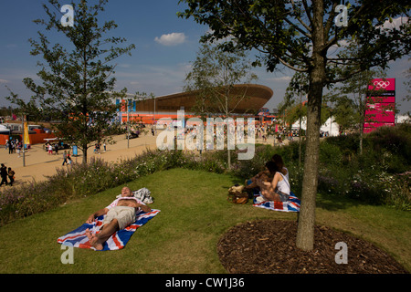 Brit spectators enjoy a hot summer on their union jack towels in the Olympic Park during the London 2012 Olympics, sitting on green grass located on a hilltop across from the iconic Velodrome venue. London’s Olympic Park, at just under a square mile, is the largest new park in the city for more than 100 years. The planting of 4,000 trees, 300,000 wetland plants and more than 150,000 perennial plants plus nectar-rich wildflower make for a colourful setting for the Games. (More captions in Description..) Stock Photo