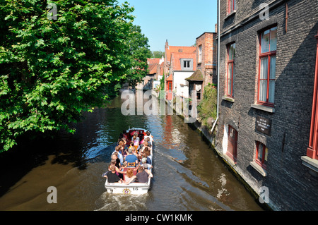 On a hot day in summer, a pleasure boat full of tourists slowly making its way along a Bruges canal. Belgium, Europe. Stock Photo