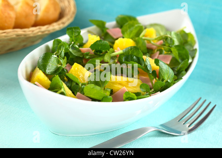 Fresh watercress, pineapple and ham salad in elongate white bowl with baguette slices in the back Stock Photo