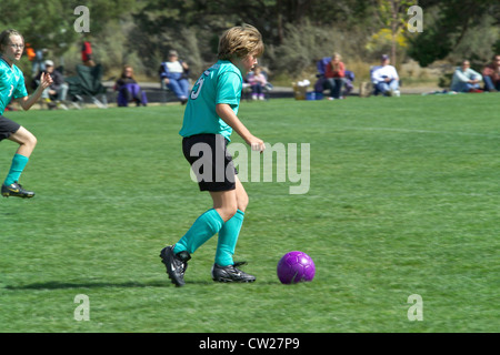 A young girl races across the playing field to kick the soccer ball during an after-school match watched by family and friends in Bend, Oregon, USA. Stock Photo